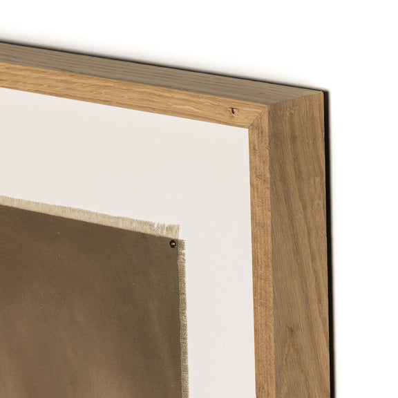 Close-up of a framed artwork corner, showing a wooden frame with a light-colored mat surrounding a darker canvas or print. The frame has a natural wood finish, emphasizing the craftsmanship of the piece.