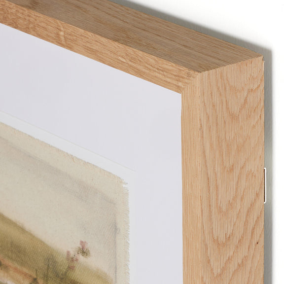 Artistic print in wooden frame, showcasing delicate watercolor landscape with soft pastel hues, mounted on white matting. Close-up view of corner detail highlighting natural wood grain texture of frame.